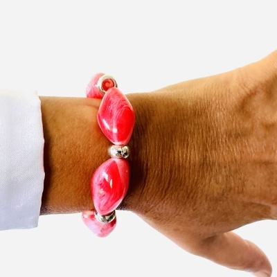 Pulseira vermelha com contas ovais e esferas prateadas num pulso