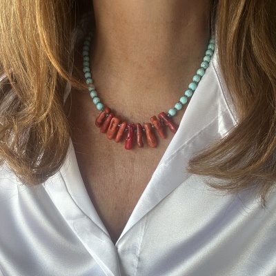 Colar azul-turquesa e vermelho em pescoço com camisa branca acetinada