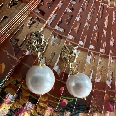 Brincos dourados com pérola sobre leque decorativo castanho e tecido floral