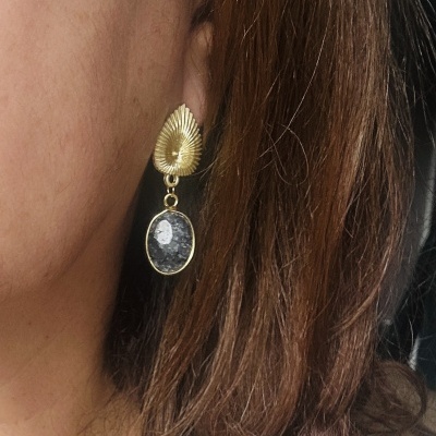 Brinco dourado com pedra cinza pendente numa orelha