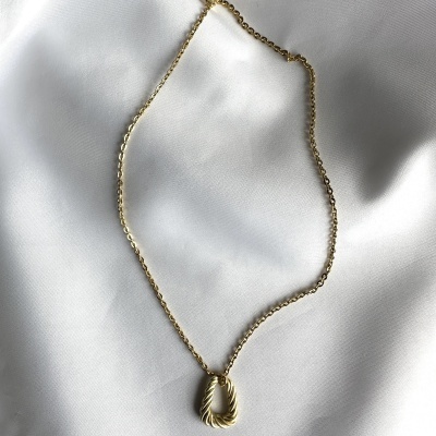 Colar dourado com pendente torcido sobre tecido branco