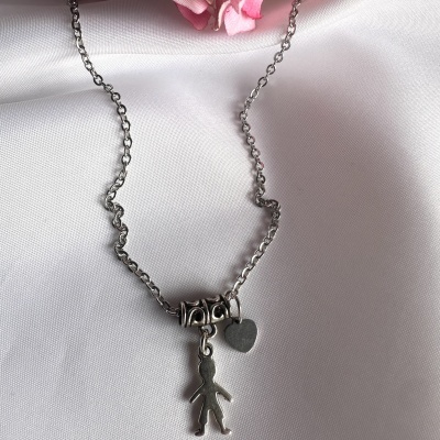 Colar de metal prateado com pendentes de figura humana e coração sobre tecido branco.