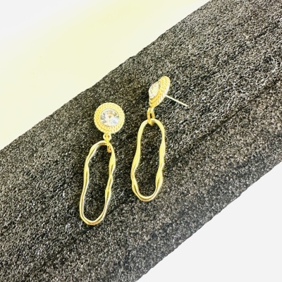 Brincos dourados com pendente e pedra transparente numa superfície texturizada cinza