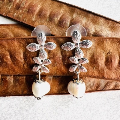 Brincos prateados com folhas e contas em forma de coração nacarado sobre couro castanho