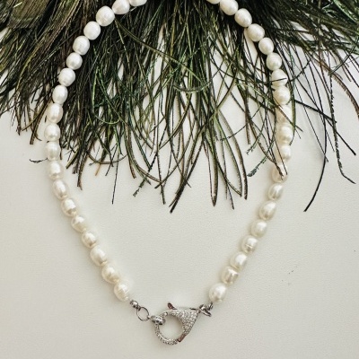 Colar de pérolas brancas com fecho prateado sobre fundo branco e penas verdes