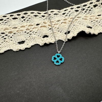 Colar com pendente de contas em forma de flor azul sobre fundo preto e renda bege