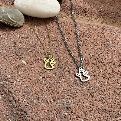 Dois colares com pendentes de anjo sobre superfície de pedra avermelhada com pedras decorativas ao fundo