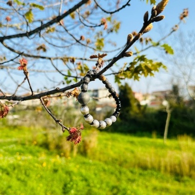 Pulseira de contas pendurada num ramo de árvore com campo verde ao fundo