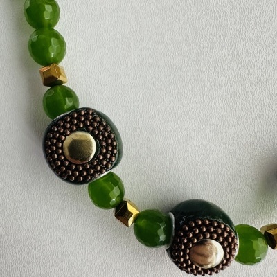 Colar com contas verdes e detalhes em bronze e dourado sobre fundo branco