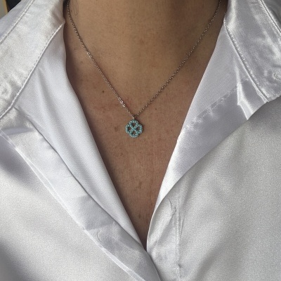 Colar prateado com pendente em forma de flor de pedras azuis num pescoço com camisa branca acetinada