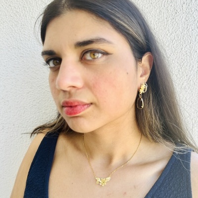 Mulher com brincos dourados ovais, colar com borboleta e vestido azul escuro