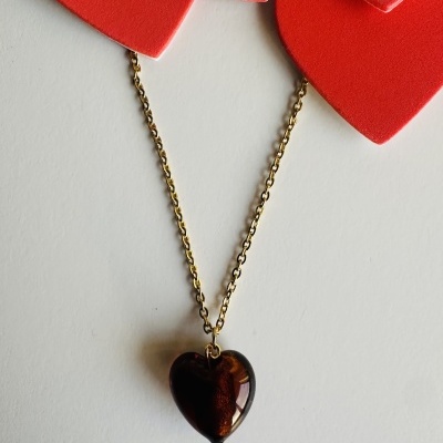 Colar com pendente castanho em forma de coração sobre fundo branco com recortes de coração vermelhos