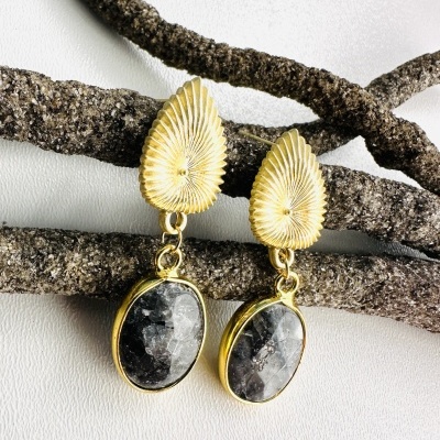 Brincos dourados com pedra oval cinza pendurados sobre galhos escuros