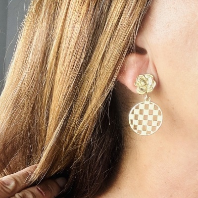 Brinco dourado floral e redondo com padrão quadriculado na orelha de mulher