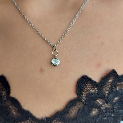 Colar prateado com pendente redondo transparente num pescoço com roupa preta de renda