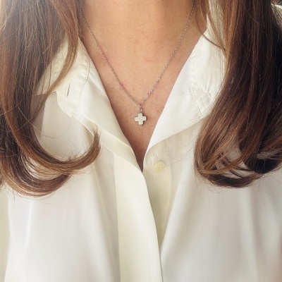 Colar prateado com pendente em cruz numa pessoa com camisa branca