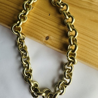 Colar dourado de corrente grossa sobre madeira e tecido branco