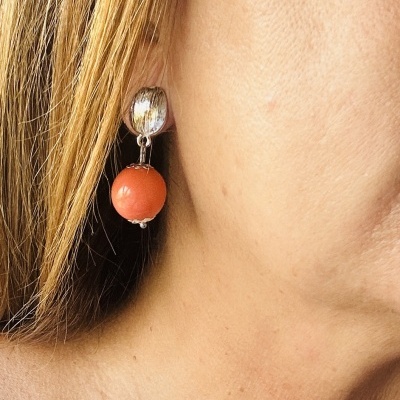 Brinco prateado com esfera laranja pendente numa orelha feminina