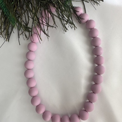 Colar de contas cor de rosa claro sobre tecido branco com folhas verdes