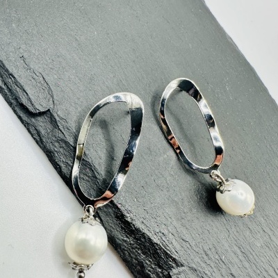 Brincos metálicos prateados com pérolas brancas sobre ardósia escura