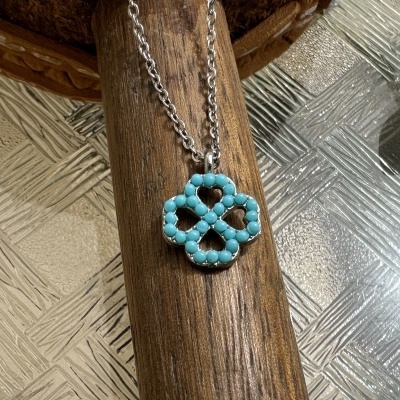 Colar com pendente de trevo turquesa e corrente prateada sobre madeira