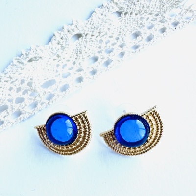 Brincos dourados com pedra azul e renda branca ao fundo