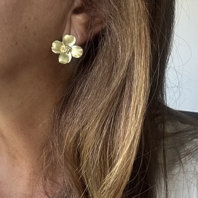 Brinco dourado em forma de flor usado na orelha