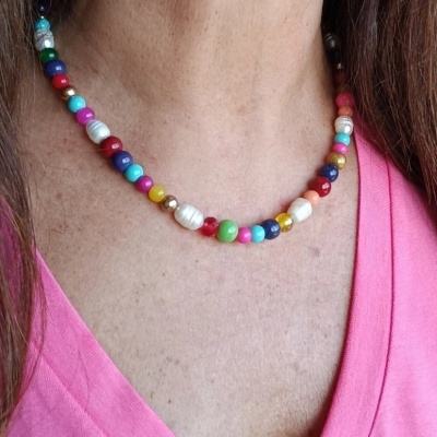 Colar colorido de contas e pérolas em pescoço de pessoa com t-shirt rosa