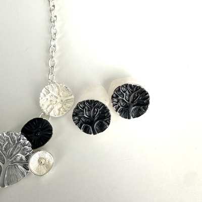Colar e anéis com pendentes redondos em metal prateado e preto com padrão de árvore.