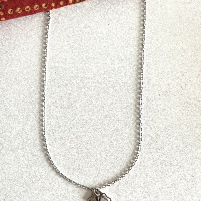 Colar prateado com pendente de trevo sobre superfície branca