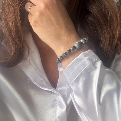 Pulseira com contas cinza e prateadas no pulso de mulher com camisa branca acetinada
