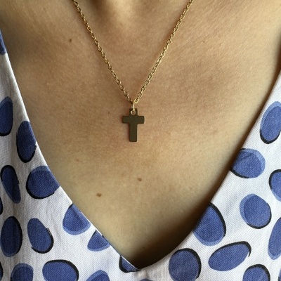 Colar dourado com pendente de cruz e vestido branco com bolinhas azuis