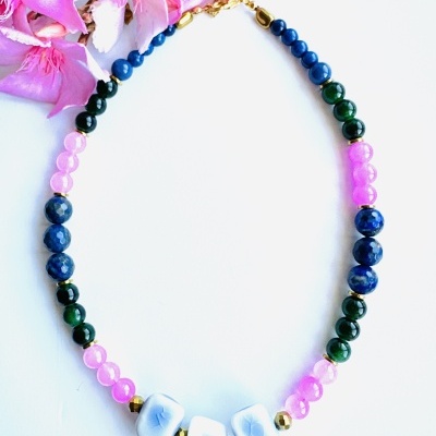 Colar com contas coloridas e flores rosas ao fundo