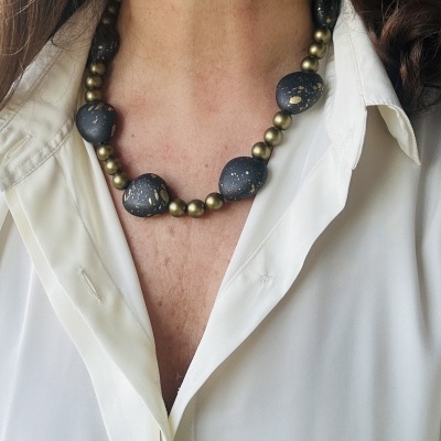 Colar com contas metálicas douradas e pedras pretas com manchas douradas sobre camisa branca
