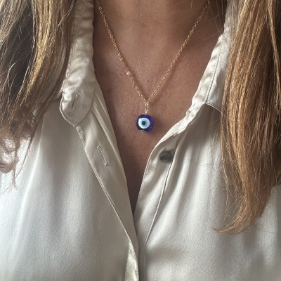 Colar com pendente azul em forma de olho turco num pescoço com camisa bege clara.