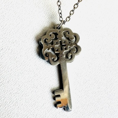 Colar com pendente chave metálica prateada e decorativa num fundo branco texturado