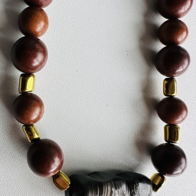 Colar com contas de madeira castanha, contas douradas e conta central em pedra preta com strias brancas
