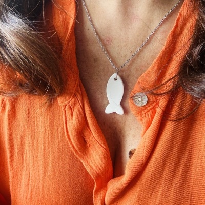 Colar com pendente em forma de peixe branco numa camisa laranja