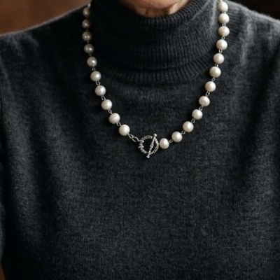 Colar de pérolas brancas com fecho circular usado numa camisola cinzenta escura