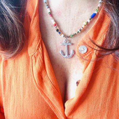 Colar com contas coloridas e pendente de âncora prateada numa blusa laranja