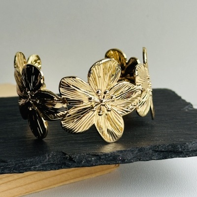 Pulseira dourada em forma de flores sobre ardósia preta