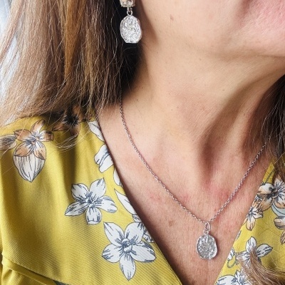 Conjunto de brincos e colar de prata com pendente texturizado em mulher com blusa amarela floral