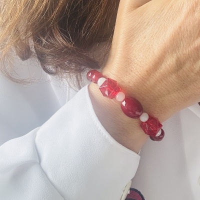 Pulseira vermelha e rosa de contas facetadas e lisas no pulso com camisa branca.