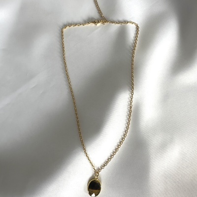 Colar dourado com pendente oval em fundo branco acetinado