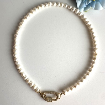 Colar de pérolas brancas com fecho dourado brilhante em superfície branca