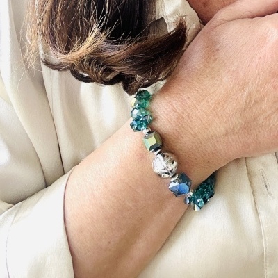 Pulseira azul e verde com contas metálicas no pulso de pessoa com camisa branca