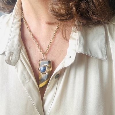 Colar pendente com pedra em tons cinza, amarelo e azul num pescoço com camisa bege clara