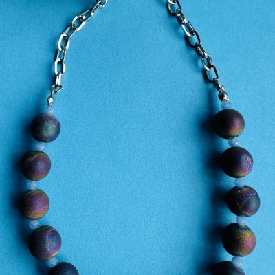 Colar com contas iridescentes e corrente prateada sobre fundo azul