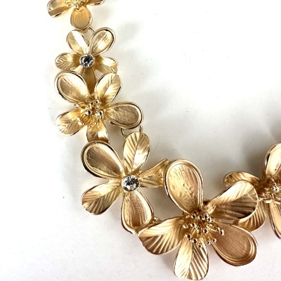 Colar de flores douradas com pedras transparentes ao centro sobre fundo branco.