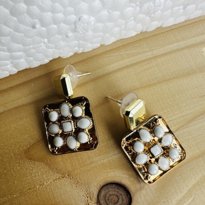 Brincos quadrados dourados com pedras brancas sobre madeira clara